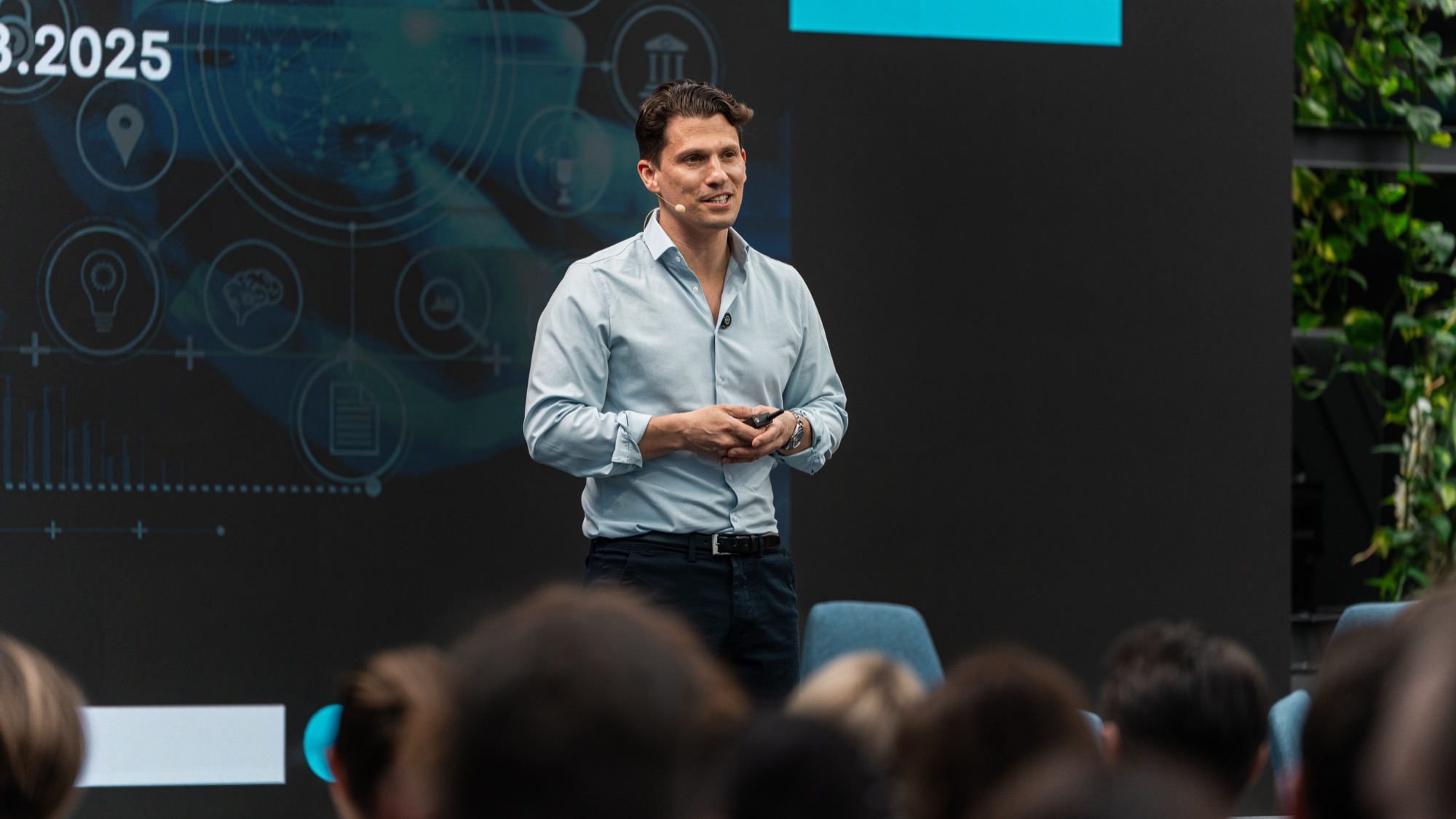 Dr. Hubertus Porschen spricht auf einer Bühne über Künstliche Intelligenz; hinter ihm eine Projektion mit KI-Symbolen, im Vordergrund die Köpfe der Zuhörenden