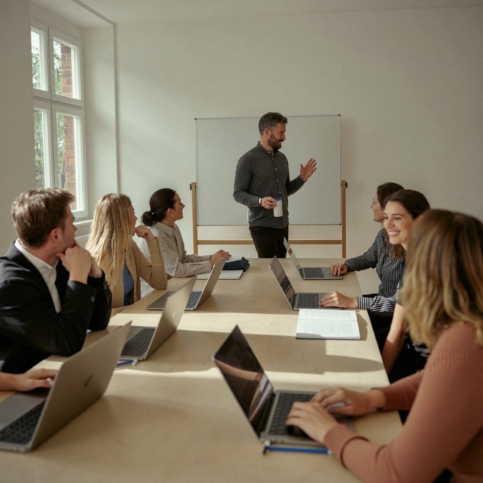 KI-Schulung in einem Mittelstandsunternehmen: ein Trainer erklärt vorne am Whiteboard, sechs Teilnehmende sitzen mit Laptops am Tisch und hören zu