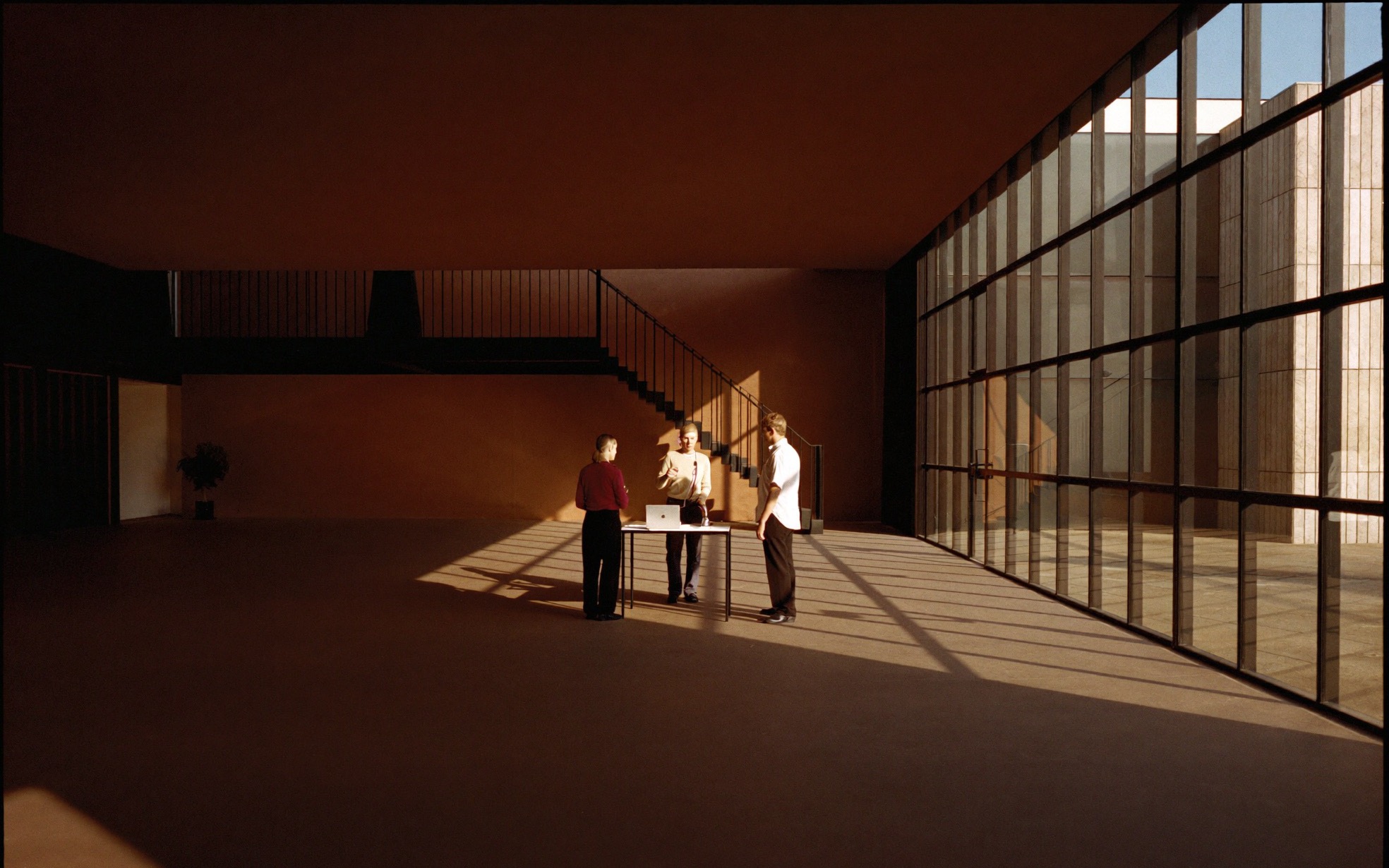 Drei Menschen stehen an einem einzelnen Tisch in der lichtdurchfluteten Halle eines modernen Firmengebäudes und besprechen die nächsten Schritte